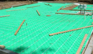 Radiant floor heating tubing laid out on a green mat, ready for concrete, by Pugh Heating & Air Conditioning in Holland, OH.