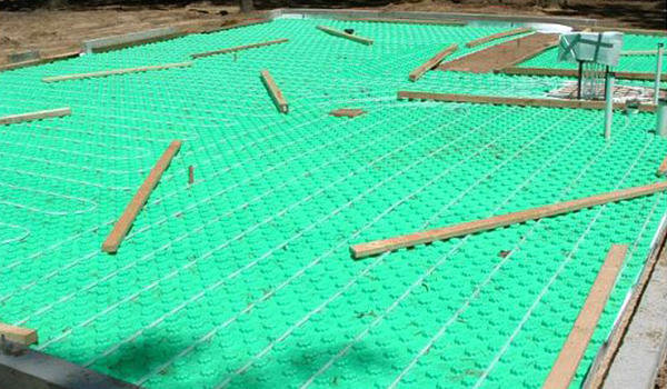 Radiant floor heating tubing laid out on a green mat, ready for concrete, by Pugh Heating & Air Conditioning in Holland, OH.