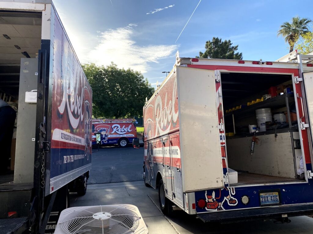 Rebel Refrigeration service trucks parked with an HVAC condenser unit in the foreground in Las Vegas, NV.