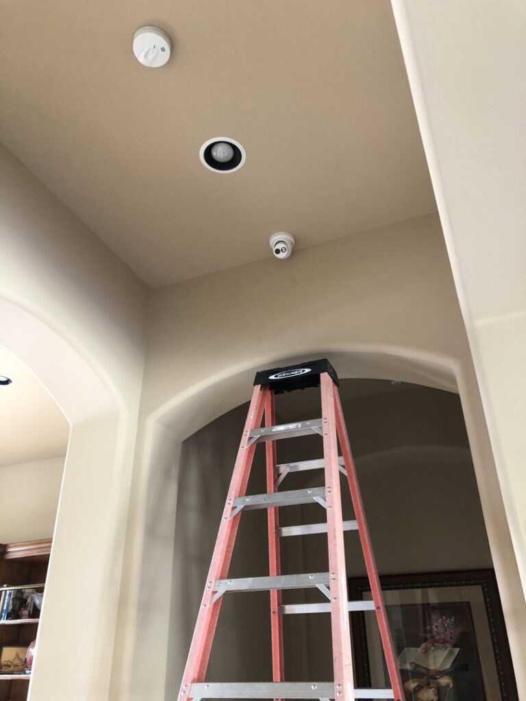 Recessed lighting, a smoke detector, and a security camera installed on a ceiling, with a ladder nearby, by PTech Installs in Columbus, GA.