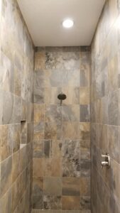 A recessed light fixture installed in the ceiling of a tiled shower by Positricity in Clearwater, FL.