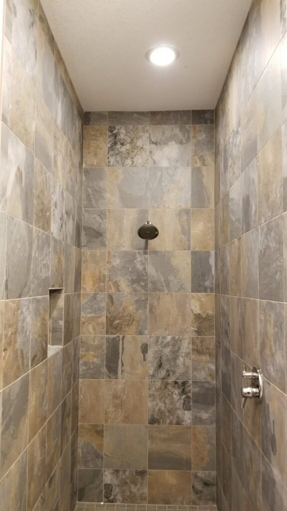 A recessed light fixture installed in the ceiling of a tiled shower by Positricity in Clearwater, FL.