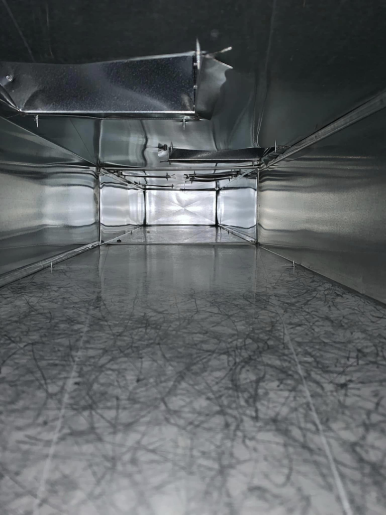 A rectangular air duct interior showing fibrous debris, indicating a need for cleaning by Air Duct Solutions in Waukee, IA.