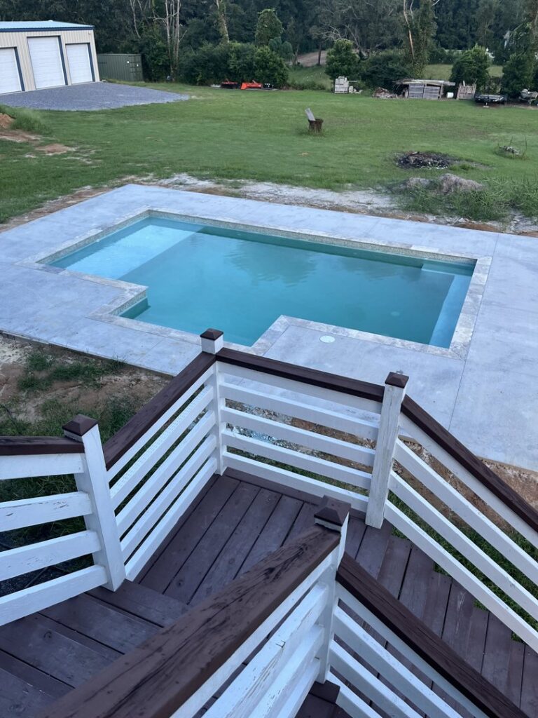 A rectangular swimming pool with clean concrete decking, viewed from an elevated deck, completed by Salty Reef Pools LLC in Summerville, SC.
