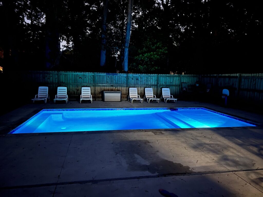 A rectangular swimming pool illuminated with vibrant blue LED lighting at night, a stunning installation by Salty Reef Pools LLC in Summerville, SC.