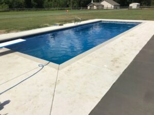 A rectangular swimming pool featuring a diving board and spacious concrete patio by Central Pools, Inc. in Baton Rouge, LA