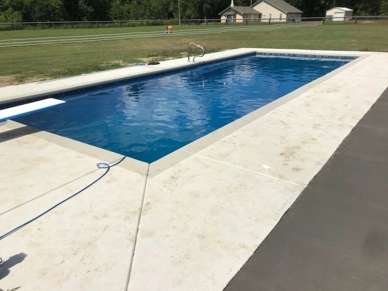 A rectangular swimming pool featuring a diving board and spacious concrete patio by Central Pools, Inc. in Baton Rouge, LA