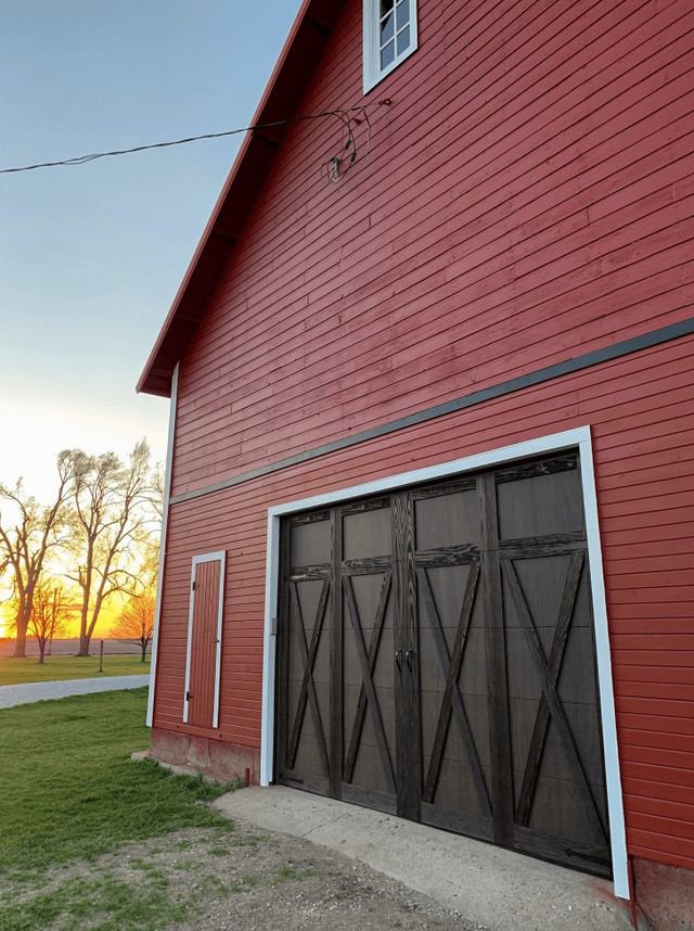 A rustic red barn featuring a dark brown carriage-style garage door installed by Monroe Overhead Doors in Monroe, LA.