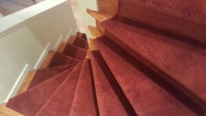 A red carpet runner installed on a spiral wooden staircase by Seattle Style Flooring in Seattle, WA.