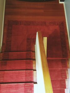 A vibrant red carpet runner professionally installed on a wooden staircase by Prestige Flooring in Auburn, AL.