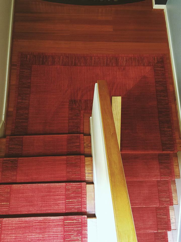A vibrant red carpet runner professionally installed on a wooden staircase by Prestige Flooring in Auburn, AL.