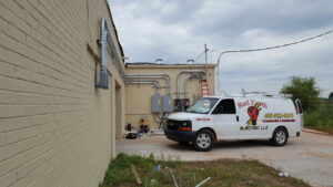 Red Earth Electric LLC van parked at a commercial electrical job site with outdoor conduit and panels in Oklahoma City, OK.