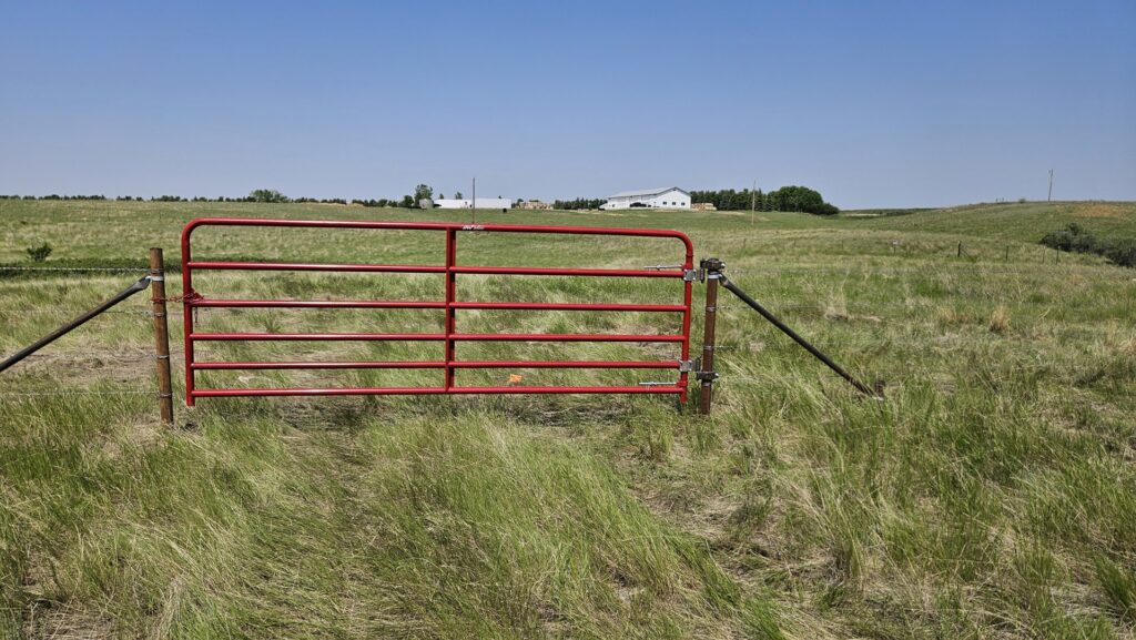 A sturdy red metal farm gate installed in a wide grassy field by Row Fencing and Services in Williston, ND.