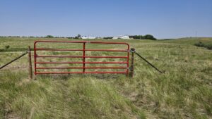 A sturdy red metal farm gate installed in a wide grassy field by Row Fencing and Services in Williston, ND.