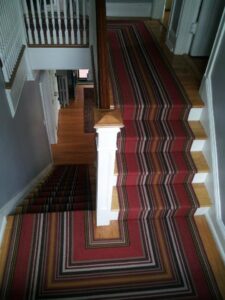 A red striped carpet runner installed on stairs and extending into a hallway by Carpet Art of America in O'Fallon, MO.