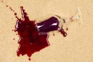 A glass of red wine spilled on a light-colored carpet, showing a stain that requires professional cleaning by Steam Giant in Raleigh, NC.