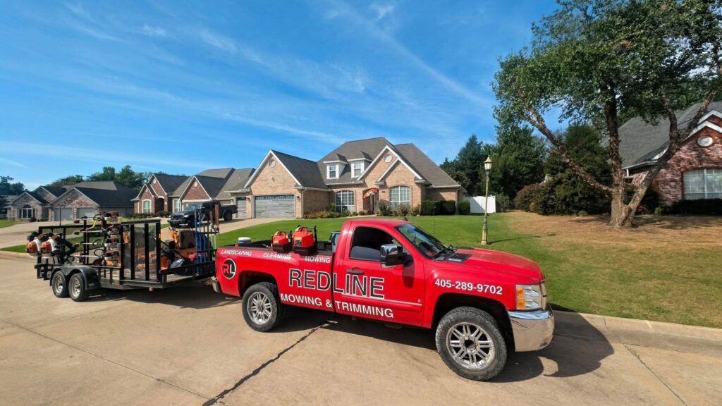 A Redline Mowing & Trimming truck with a trailer full of professional lawn care equipment parked in a residential neighborhood in Stillwater, OK.