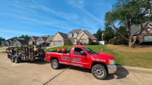 A Redline Mowing & Trimming truck with a trailer full of professional lawn care equipment parked in a residential neighborhood in Stillwater, OK.