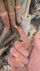 A hand pointing to a brass fitting on a copper refrigerant line of an outdoor AC unit by Quantum Cooling & Heating in Mesa, AZ.