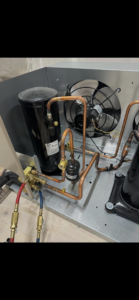 Close-up of a refrigeration system's compressor, copper piping, and fan, indicating service by Kusi.aat' Kaa' Refrigeration in Homer, AK.