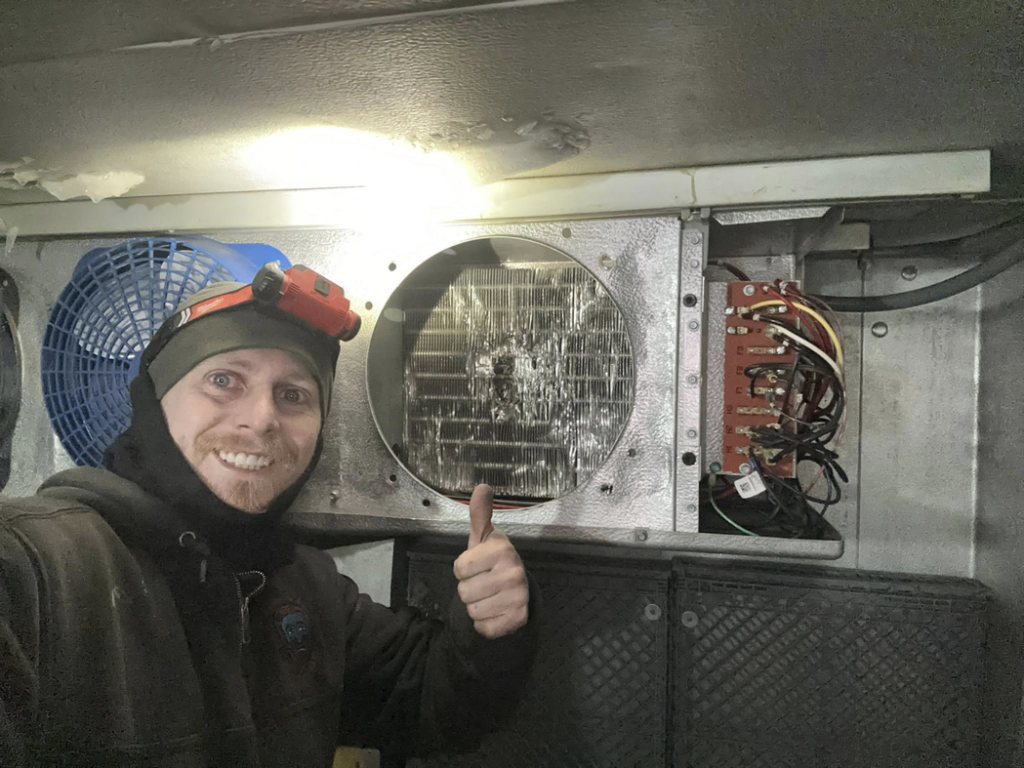 A refrigeration technician from Kusi.aat' Kaa' Refrigeration giving a thumbs-up while working inside a walk-in freezer in Homer, AK.
