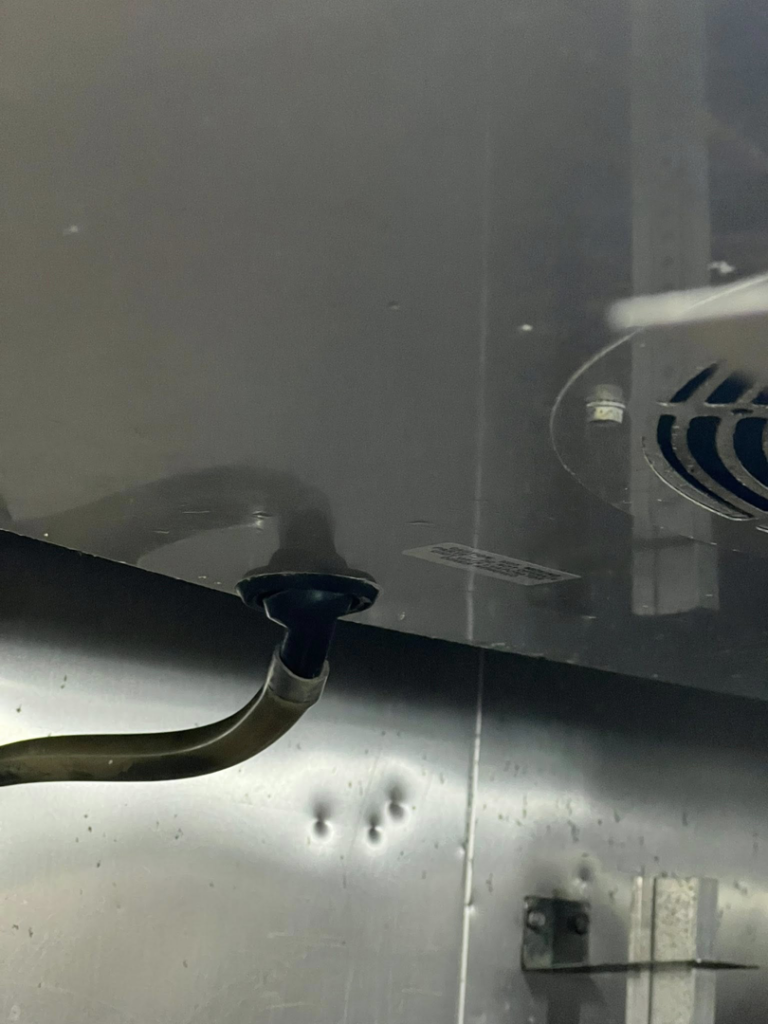 A close-up view of a refrigeration unit component with a pipe and fan, serviced by Kusi.aat' Kaa' Refrigeration in Homer, AK.