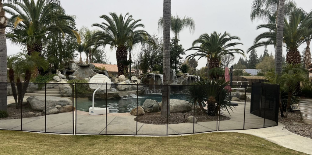 A durable removable pool safety fence installed around a backyard swimming pool with a rock waterfall by A Safe Pool Enclosures in Bakersfield, CA.
