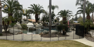 A durable removable pool safety fence installed around a backyard swimming pool with a rock waterfall by A Safe Pool Enclosures in Bakersfield, CA.