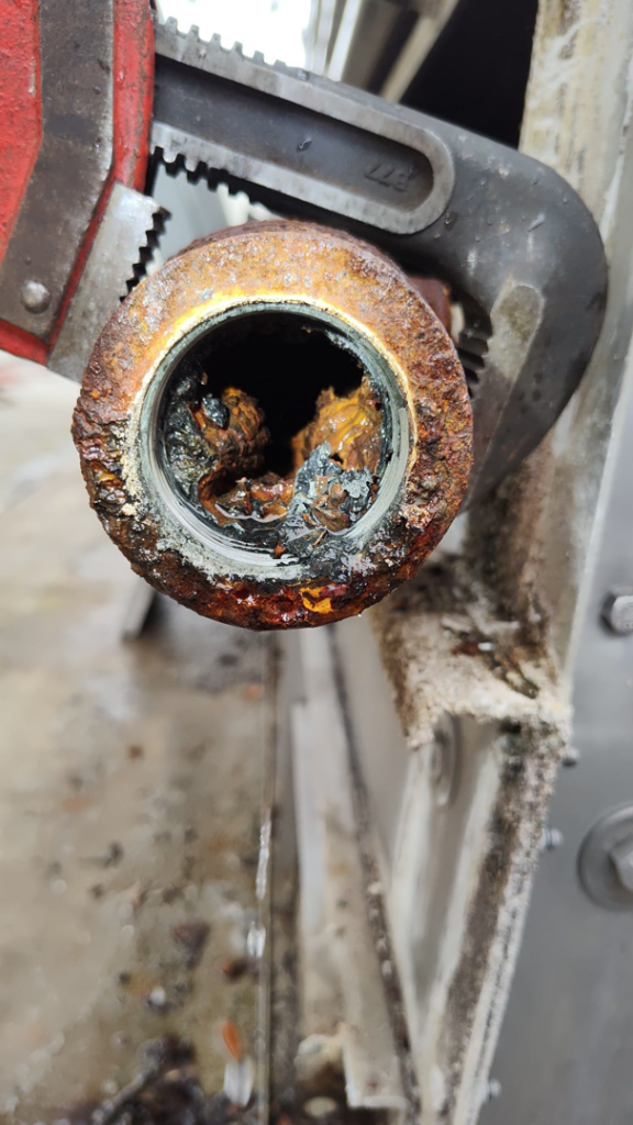A pipe wrench used to remove a severely clogged and corroded pipe section during HVAC system maintenance by CMC Mechanical in Goose Creek, SC.
