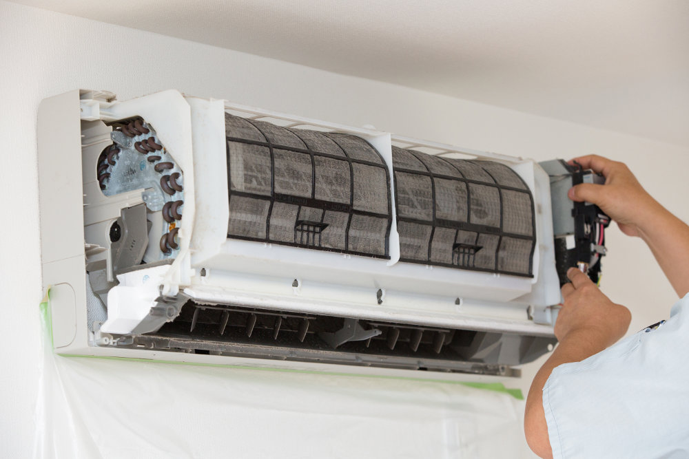 A person removing a dirty filter from an indoor split AC unit for Glendale HVAC in Glendale, AZ
