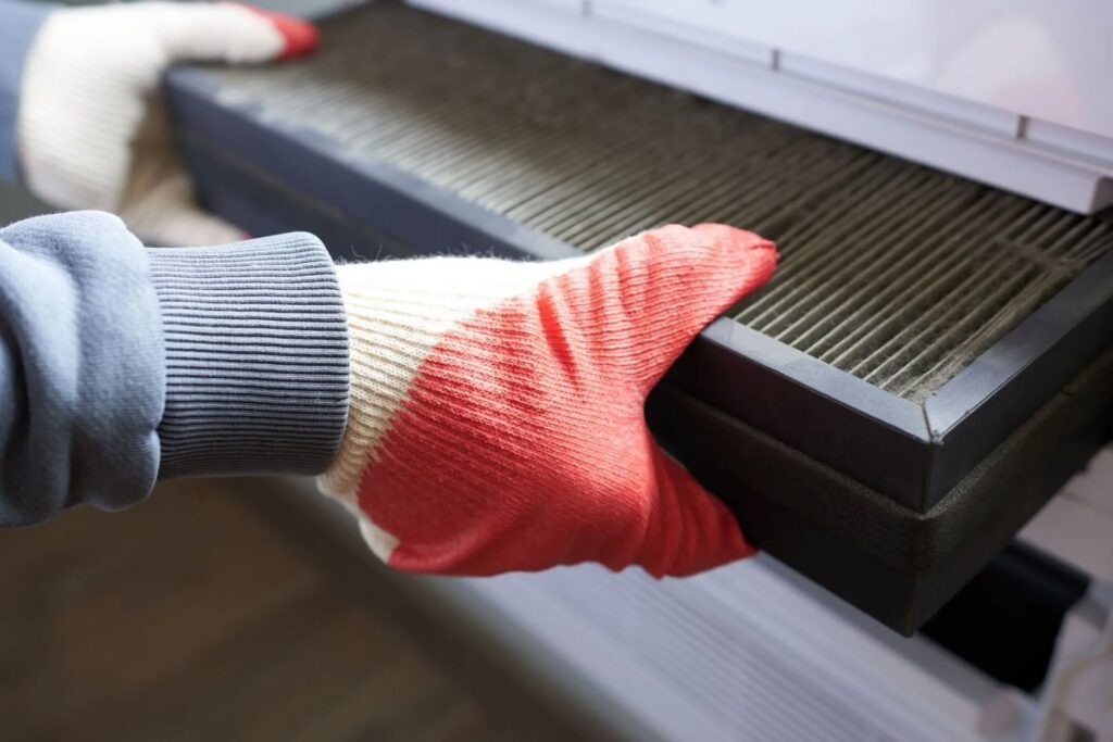 Hands in gloves removing a dirty air filter from an HVAC unit during maintenance by Ault's Cooling HVAC Services LLC in Chandler, AZ.