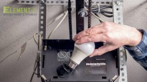 A hand replacing a light bulb in a garage door opener, a common repair by Element Garage Door Repair Of Portland, OR
