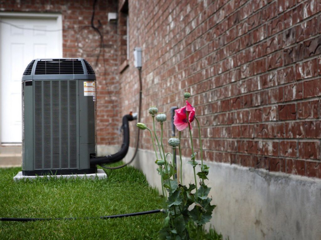 A residential outdoor air conditioning unit next to a brick house, installed by Reliance Home Comfort in Hampton, VA.