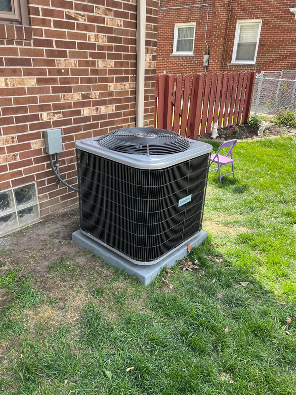 A residential outdoor AC unit installed on a concrete pad next to a brick home by Motown Mechanical Heating And Cooling in Westland, MI.