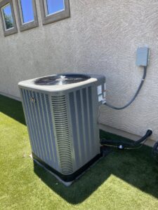 A residential AC condenser unit installed on artificial turf next to a house by J & M Cooling & Heating LLC in Peoria, AZ.
