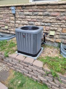 A residential AC unit installed next to a decorative stone wall by Kraemer Mechanical in Broomfield, CO.
