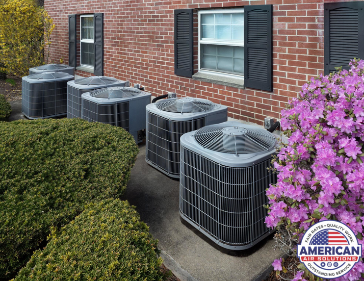 A row of outdoor residential air conditioning units installed alongside a brick house, maintained by American Air Solutions in Summerville, SC.