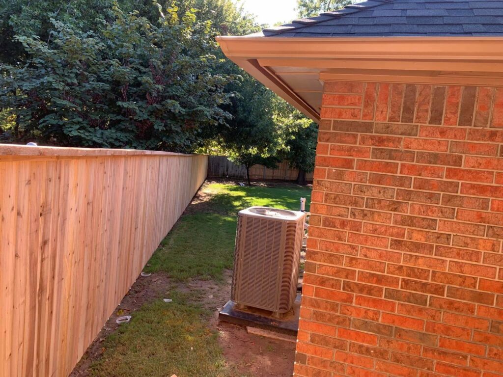 A newly installed wooden privacy fence in a residential backyard, next to an AC unit, by TOP TIER FENCE LLC in Oklahoma City, OK.