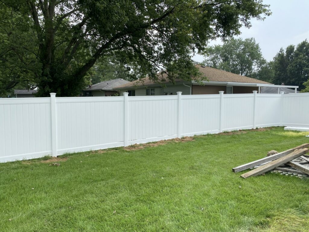 A white vinyl fence enclosing a residential backyard with green grass by Nailed It Fencing and Exteriors in Evansville, IN.