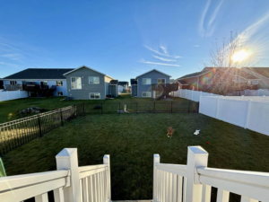 An expansive residential backyard enclosed by a black ornamental fence and a white vinyl fence, installed by VASE Construction, LLC in Fargo, ND.