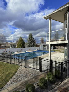 A residential backyard featuring a black metal pool fence and a white privacy fence installed by BKC Fencing in Spokane, WA.