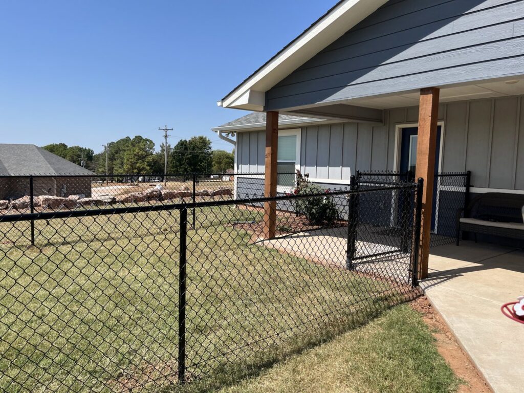A black chain link fence installed around a residential property by 12 Corners Fence Company in Tecumseh, OK