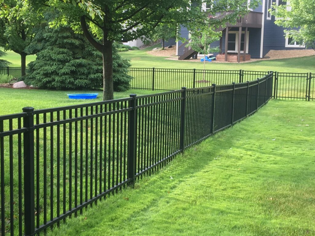 A residential black metal fence enclosing a lush green backyard, installed by Mauer Company in Little Canada, MN.