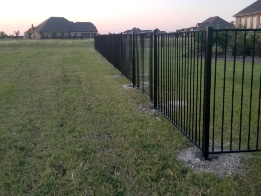 A long black metal residential fence installed by Dallas Mobile Welder, LLC. in a Dallas, TX backyard.