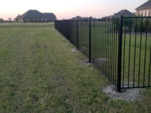 A long black metal residential fence installed by Dallas Mobile Welder, LLC. in a Dallas, TX backyard.