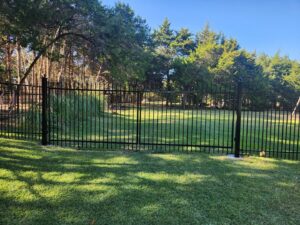 A residential black metal fence and gate in a grassy yard, installed by Iron Fence Services, LLC in Lancaster, TX.