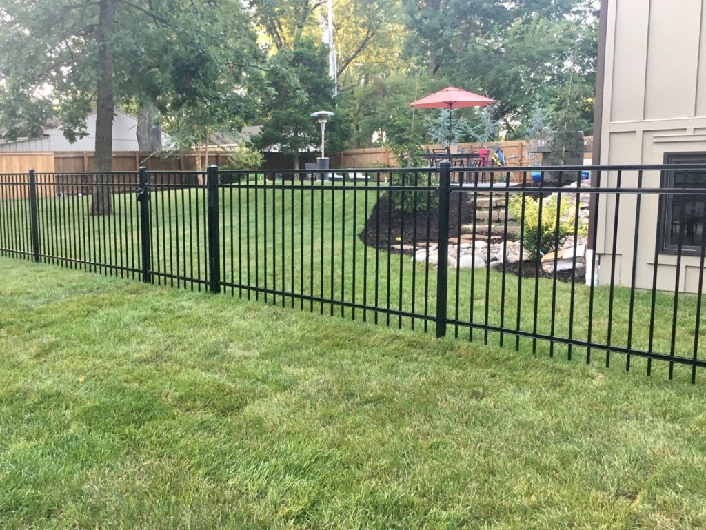 A residential backyard enclosed by a new black ornamental iron fence installed by Roy & Son Fencing in Lee's Summit, MO.