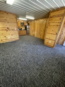 New residential carpet installed in a room with wood paneling and a small kitchen area by Rayman Flooring in Aberdeen, SD