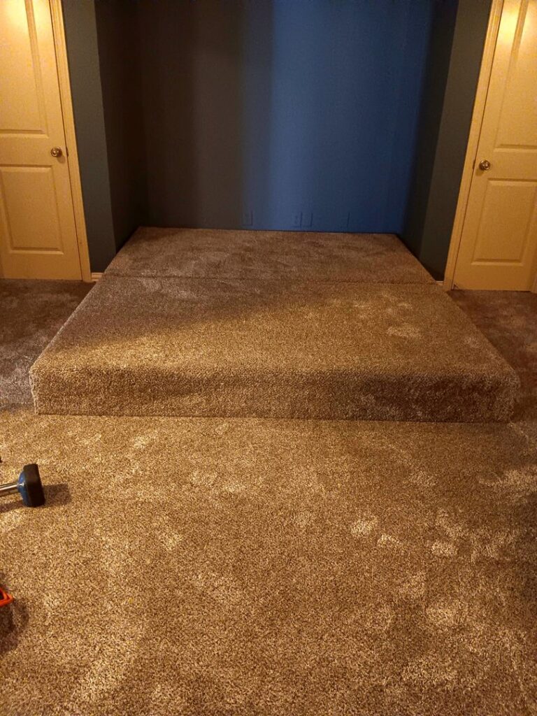 Brown residential carpet installed in a room, including a custom-carpeted raised platform, by Affordable Carpet & Flooring in Dallas, TX.