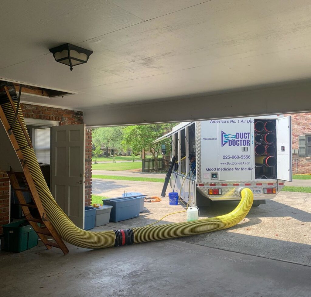 Residential air duct cleaning setup with a large yellow hose connecting the attic to a service truck from Duct Doctor of Baton Rouge, LA.